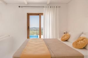 a white bedroom with a large bed and a window at Akrolithos Villas in Kouvaláta