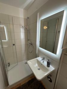 ein Bad mit einem Waschbecken und einer Dusche mit einem Spiegel in der Unterkunft Ferienwohnung 1 Zimmer App Ankerplatz 43 im Olympiazentrum in Kiel