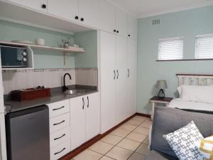 cocina con armarios blancos, fregadero y cama en NoniSands Guesthouse, en Uvongo Beach