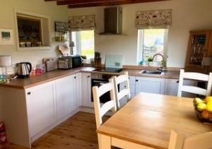 a kitchen with white cabinets and a wooden table with chairs at Bizzys Place in Gunnerside
