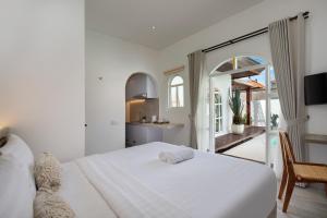 a white bedroom with a large bed and a kitchen at Kemari Studio in Canggu