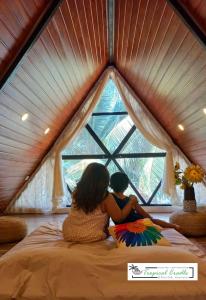 a woman and a child sitting on a bed looking out a window at Tropical Cradle @ River Dale in Kalyānpur