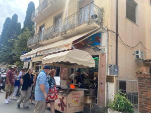 a group of people standing outside of a food stand at Tauromenium House in Taormina