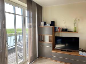a living room with a television and a balcony at Ferienhaus Grodenblick Sanddorn Whg 3 in Wangerooge