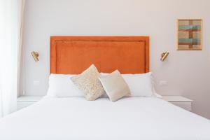 a white bed with white pillows and an orange headboard at Daplace - Gran Torino Suites in Rome