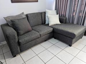 um sofá cinzento com almofadas num piso de azulejo branco em @Kitchens em Jeffreys Bay