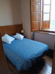 Schlafzimmer mit einem Bett mit blauer Bettwäsche und einem Fenster in der Unterkunft Apartamentos Rurales San Esteban de los Buitres - Illano 