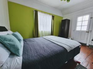 Un dormitorio con una cama con paredes verdes y una ventana en Meraki Hostel - Cerro Alegre - Valparaíso en Valparaíso