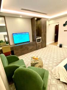 sala de estar con sillas verdes y TV de pantalla plana en Narmiss Aparthotel, en Unaizah