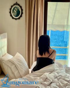 Eine Frau, die auf einem Bett sitzt und aus dem Fenster schaut. in der Unterkunft Hotel Lungomare in Vlorë