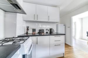 a white kitchen with white cabinets and a stove at Contemporary 4 bedroom detached house with parking and city links in Croydon