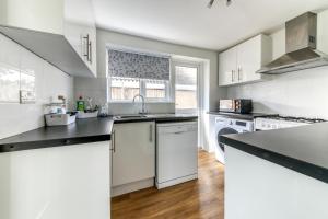 a kitchen with white cabinets and a white dishwasher at Contemporary 4 bedroom detached house with parking and city links in Croydon