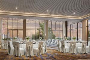 um salão de banquetes com mesas e cadeiras brancas e janelas grandes em Courtyard by Marriott Ahmedabad Sindhu Bhavan Road em Ahmedabad