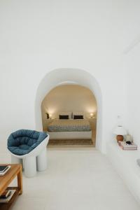 a white bedroom with a bed and a blue chair at Kalyva Cycladic house - Oia Santorini in Oia