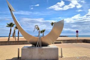 une sculpture sur une plage avec des palmiers et l'océan dans l'établissement Gîte VILLA 34 Résidence Le Grand Bleu, à Vendres