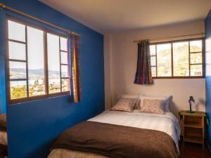 um quarto com paredes azuis e uma cama com 2 janelas em HOSTAL Casa Verde em Otavalo
