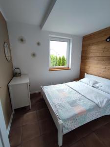 1 dormitorio con 1 cama con cabecero de madera y ventana en SOWI KĄT domki i apartamenty en Mikołajki