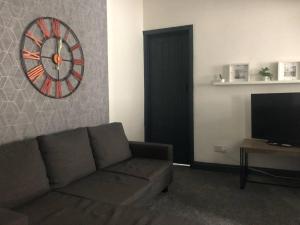 a living room with a couch and a clock on the wall at Stainsby House 4 Bedrooms Workstays UK in Stockton-on-Tees