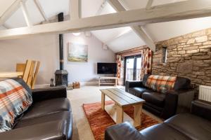 sala de estar con muebles de cuero y pared de piedra. en Round Knott, Sebergham, Nr Caldbeck, en Sebergham