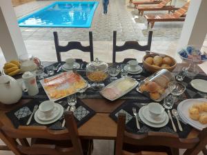 a table with breakfast food and a swimming pool at Pousada Ninhal das Garças in Ilha Comprida