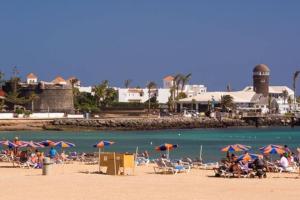 a group of people sitting on a beach with umbrellas at Piscina & Wifi. SUNNY apartement, swimming pool. in Caleta De Fuste