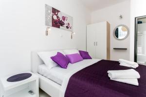 a white bedroom with a large bed with purple pillows at Apartment Purple Magic in Dubrovnik