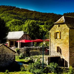 un edificio de piedra con sombrillas rojas y un restaurante en Chambres d'hôtes Microbrasserie & Auberge Ortan, en La Canourgue