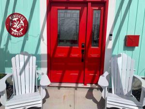 zwei weiße Stühle vor einer roten Tür in der Unterkunft Hibiscus House in Stratford