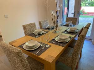 a wooden table with chairs and plates and wine glasses at Burton - 4 Bedroom Detached Home in Shenley Church End