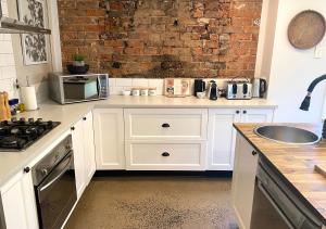 una cocina con armarios blancos y una pared de ladrillo en The Edward Townhouses 151 & 153, en Orange