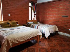 two beds in a room with a brick wall at Kalera Wasi in Cotacachi