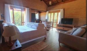 a bedroom with a bed and a couch and a tv at Chalé Caminho do Paiol in São Bento do Sapucaí