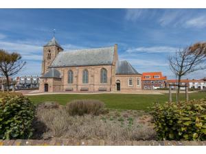 a large brick church with a tower on a field at Enjoy a holiday in the cozy Tiny house on the edge of the forest and the dunes! in Zoutelande