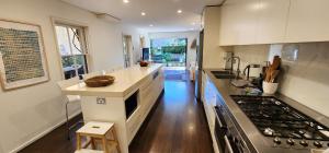 La cuisine est équipée de placards blancs et d'un four avec plaques de cuisson. dans l'établissement Grand Terrace With Secret Garden - 4 Bedrooms, à Sydney