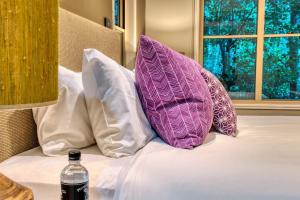 Una cama con almohadas moradas y blancas y una botella de agua. en Narrows Escape Rainforest Retreat en Montville