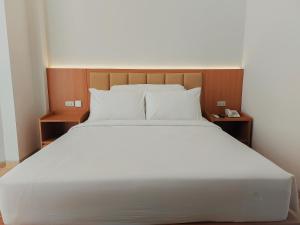 uma cama grande com lençóis brancos e almofadas em AYMAN SYARIAH HOTEL em Surabaia