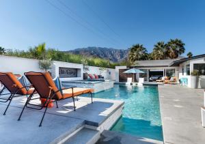 a backyard with a swimming pool with chairs and a fireplace at Luxury Desert Oasis in Palm Springs