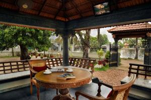 a wooden table and chairs on a patio at The Backwater Heritage- Comp Breakfast with River View & Lawn by StayVista in Alleppey