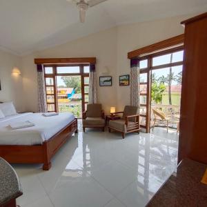 a bedroom with a bed and two chairs and sliding glass doors at Sunset Beach Resort in Candolim
