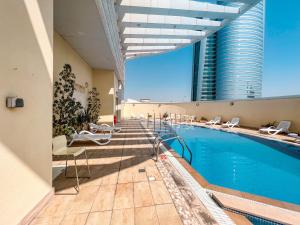 a hotel swimming pool with chairs and a tall building at Cosmos Living Luxurious Studio Near Metro in Dubai