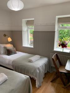 a bedroom with two beds and a desk and two windows at The Old Dairy at Walkmill Farm in Bushmills