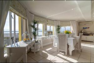 uma cozinha com mesas e cadeiras brancas e janelas em Gordon's Beach Lodge em Gordonʼs Bay