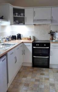 a kitchen with white cabinets and a black oven at Little Garden Cottage, Tamar Valley, Cornwall in Stoke Climsland