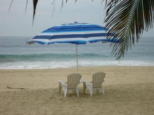 two chairs under an umbrella on the beach at Condominio Gaudi in Pie de la Cuesta