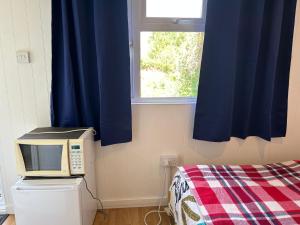 a room with a microwave and a bed with blue curtains at Mini cabin in Zone 2 in London