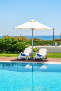 Dos sillas y una sombrilla junto a una piscina. en Seafront Villa Maya by Ruidoso Luxury, en Ayia Napa