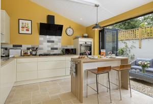 eine Küche mit gelben Wänden und einer Theke mit Hockern in der Unterkunft Rock Cottage in Minchinhampton + 14 Fotos