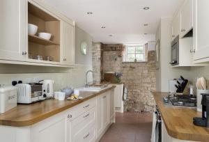 a kitchen with white cabinets and a stone wall at Southcroft Cottage in Bredon
