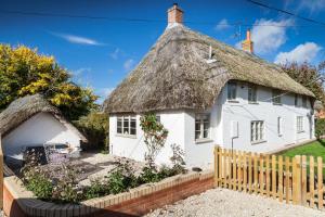 a small white cottage with a thatched roof at Wisteria Cottage in Urchfont