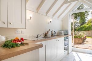 Densford Cottage في أَمبيرلي: مطبخ مع خزائن بيضاء ووعاء من الخضروات على منضدة